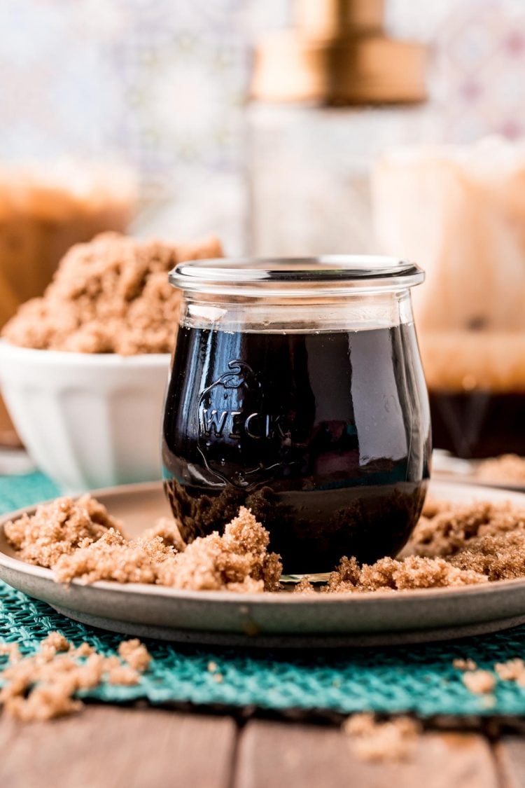 Close up photo of a jar of brown sugar simple syrup on a brown plate with brown sugar all around it.