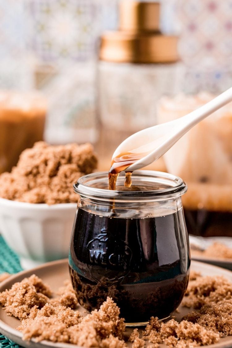 Close up photo of a white spoon spooning brown sugar simple syrup out of a jar.