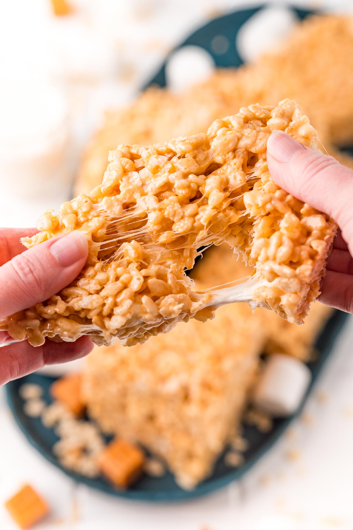 Caramel rice krispie treat being pulled apart by a woman's hands.