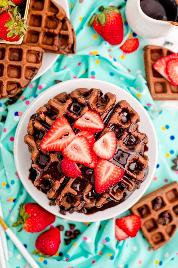 Overhead photo of a stack of chocolate waffles topped with chocolate syrup and strawberries.