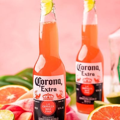 Close up photo of a Corona sunrise in a Corona bottle with citrus and palm leaves around it.
