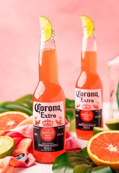 Close up photo of a Corona sunrise in a Corona bottle with citrus and palm leaves around it.