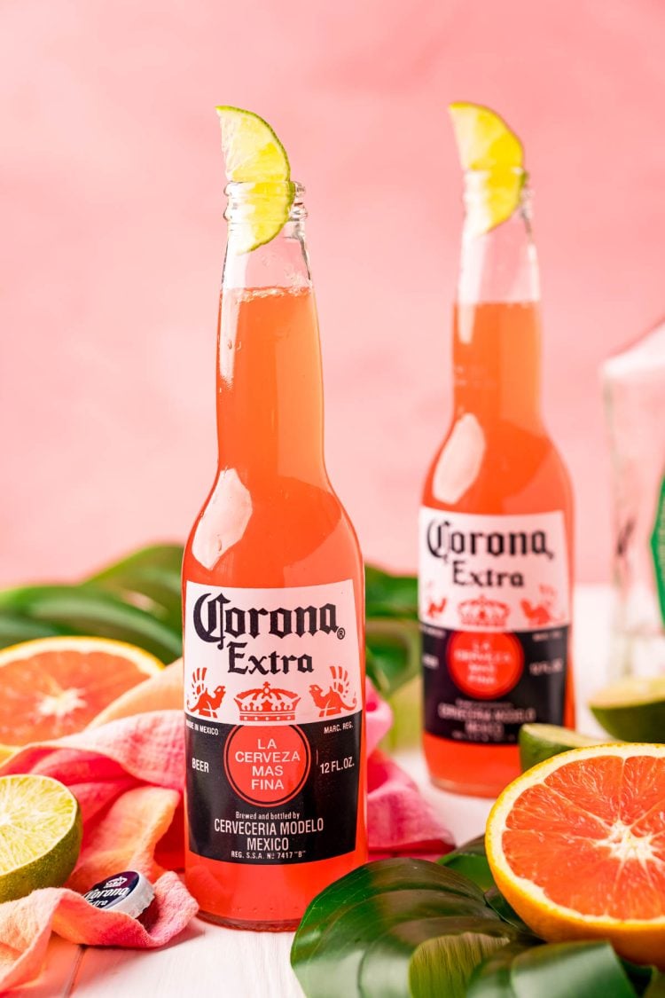 Close up photo of a Corona sunrise in a Corona bottle with citrus and palm leaves around it.