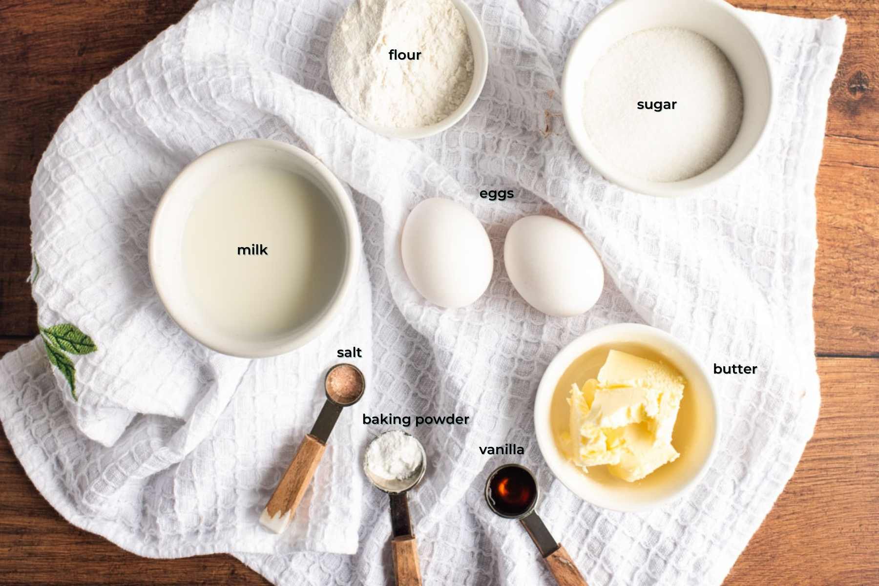Ingredients used to make donut cookies arranged on a white kitchen towel on a wooden table.