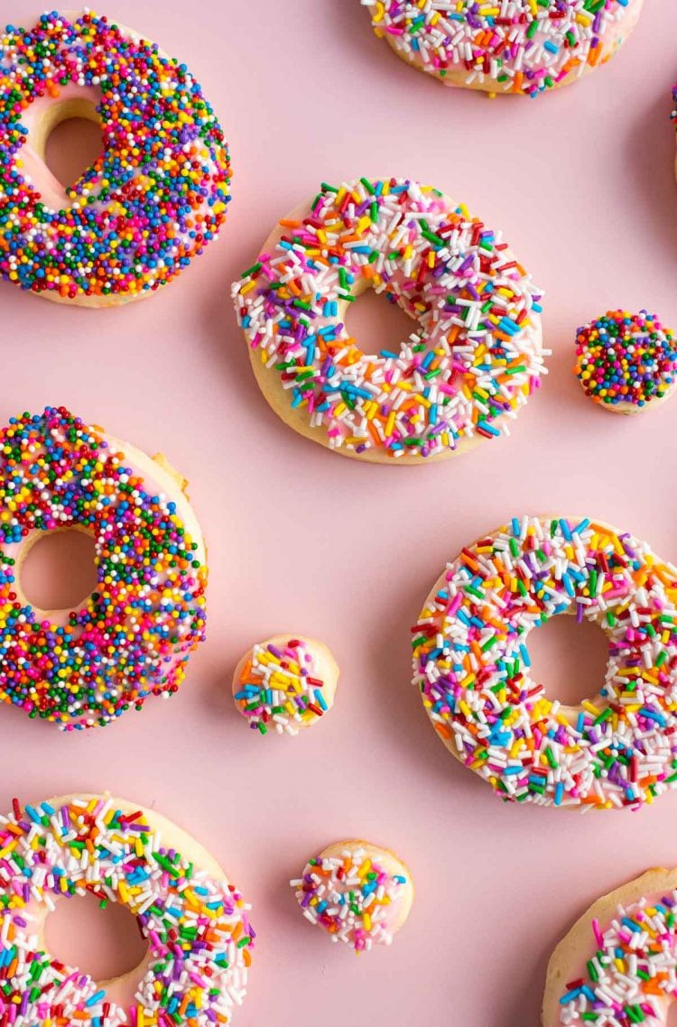 Overhead photo of donut cookies spread out on a pink surface.