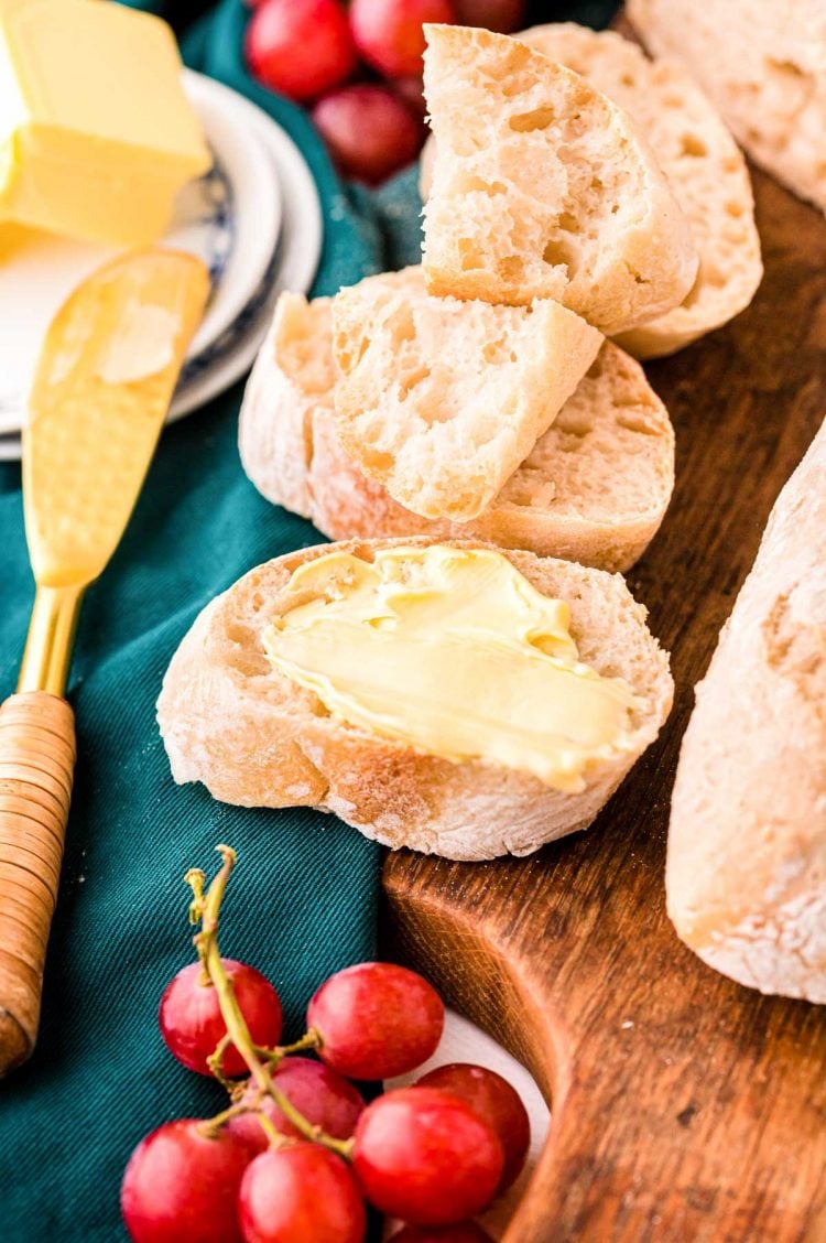 Close up photo of slices of baguette bread with butter and grapes around.