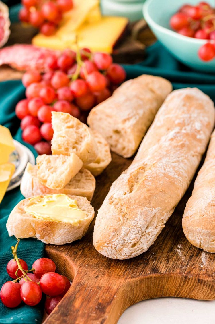 French Baguettes on a wooden cutting board, one has been sliced up and has butter on it.