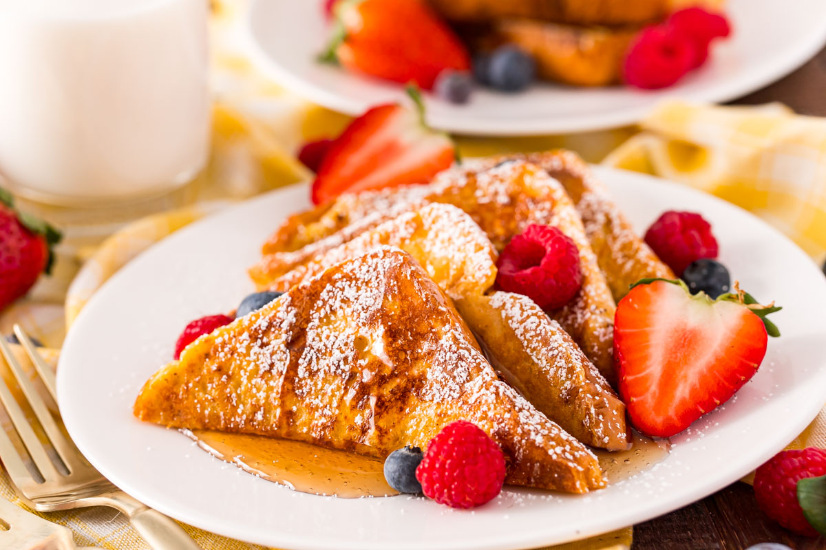 Close up photo of French toast on a white plate with berries.