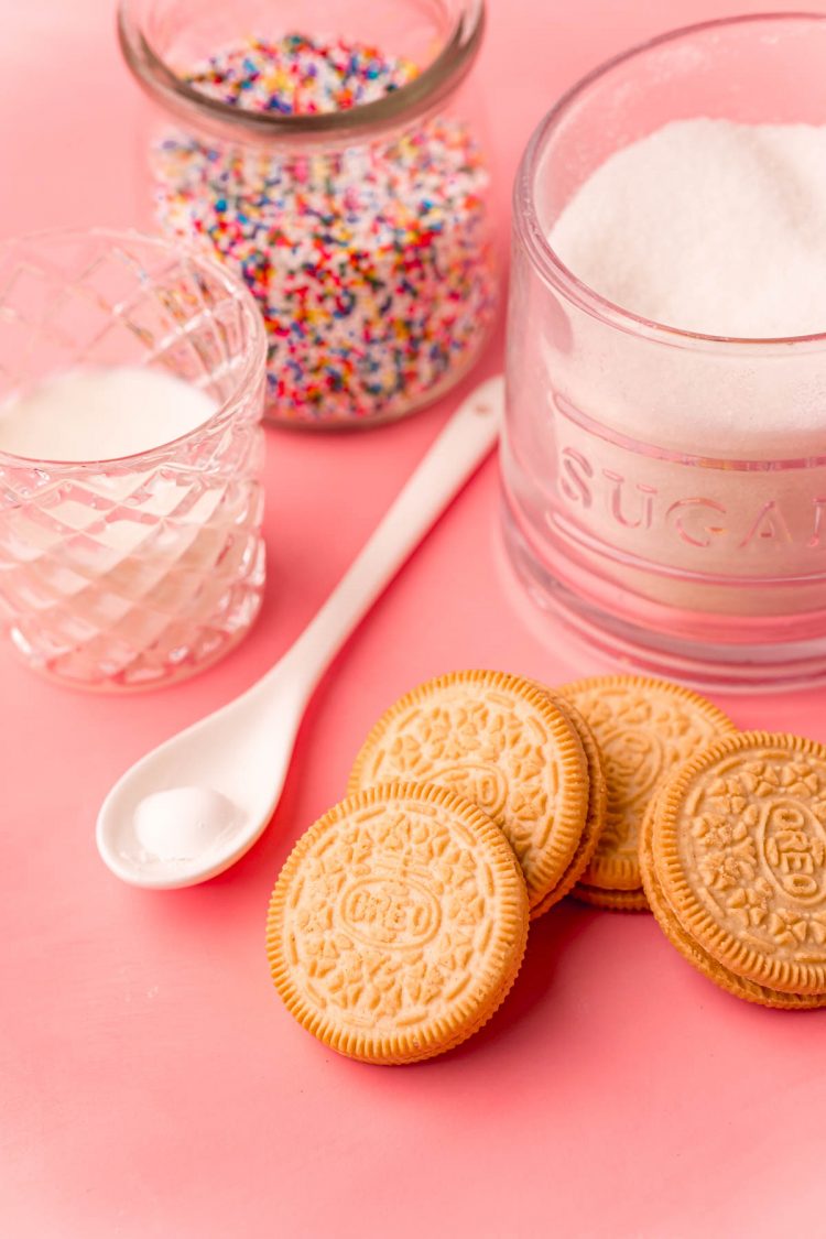 Ingredients to make a mug cake with golden Oreos on a pink surface.