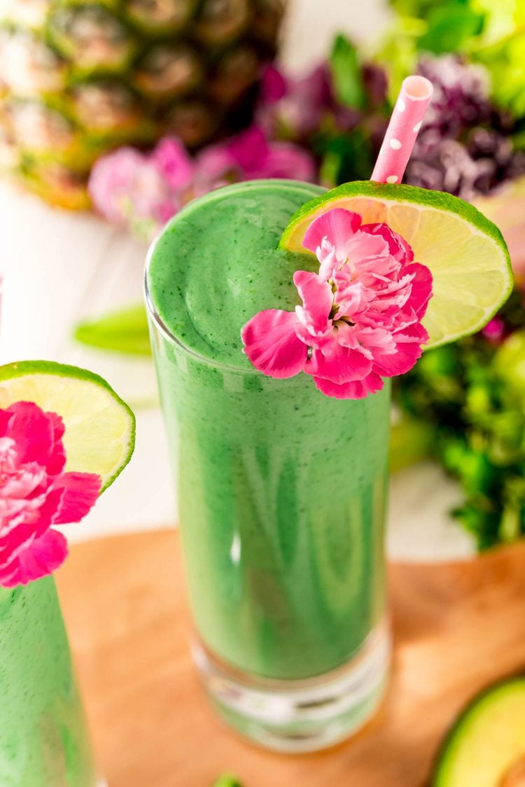 Close up photo of green smoothie with a pink carnation, lime slice, and pink straw.