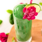 Close up photo of a green smoothie in a tall glass garnished with a pink carnation and lime slice.