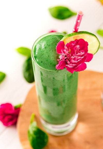 Close up photo of a green smoothie in a tall glass garnished with a pink carnation and lime slice.