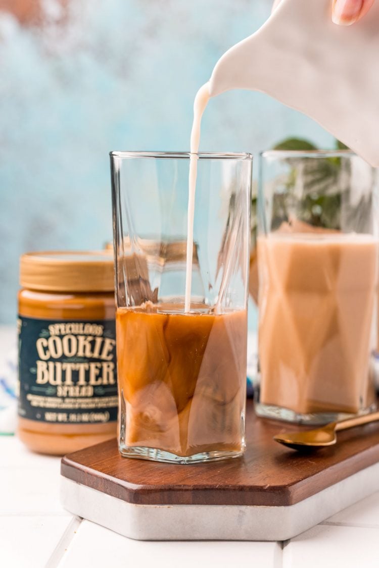 Oat milk being poured into a tall glass to make a cookie butter latte.