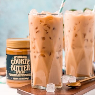 Straight on photo of two glasses filled with iced cookie butter lattes and a jar of cookie butter next to it.