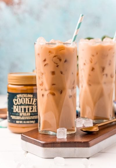 Straight on photo of two glasses filled with iced cookie butter lattes and a jar of cookie butter next to it.