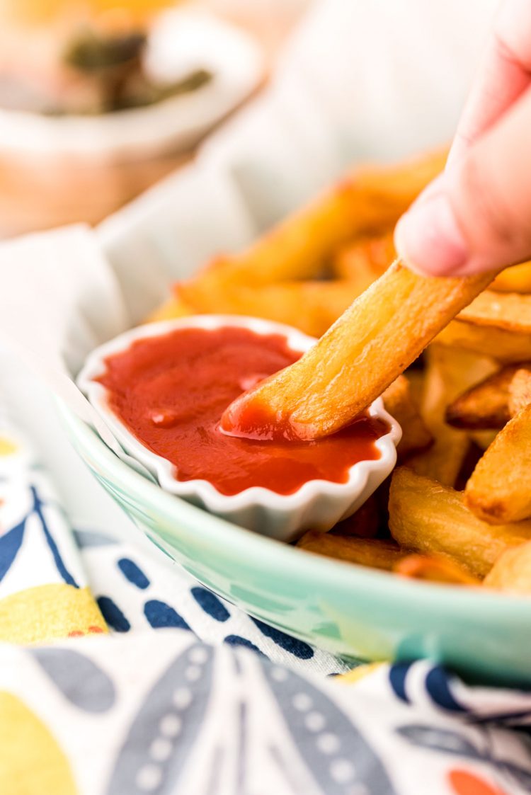 Close up photo of a hand dipping a French fry in ketchup.