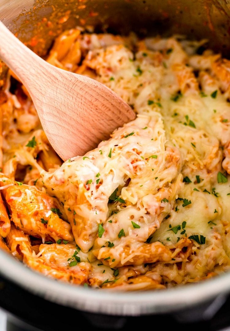 Close up photo of a wooden spoon scooping into an instant pot with chicken parmesan pasta in it.