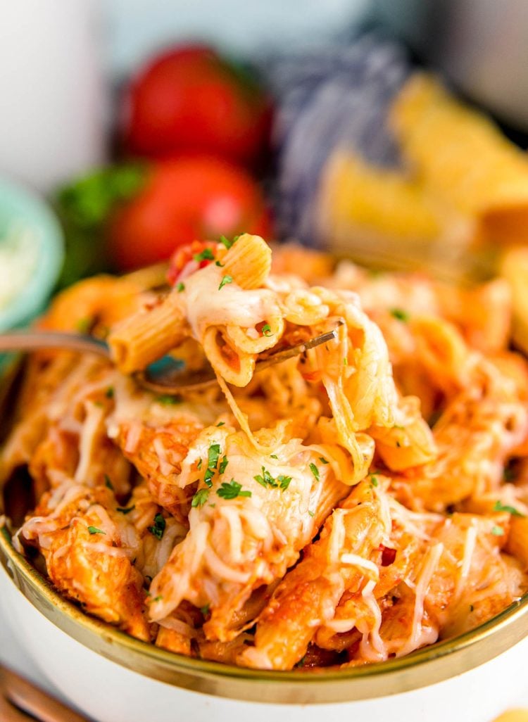 Close up photo of a fork taking a bite of chicken parm pasta out of a bowl.