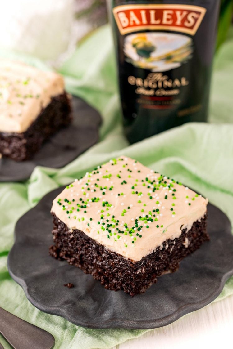 Irish cream cake slice on a black plate with a bottle of Bailey's in the background.