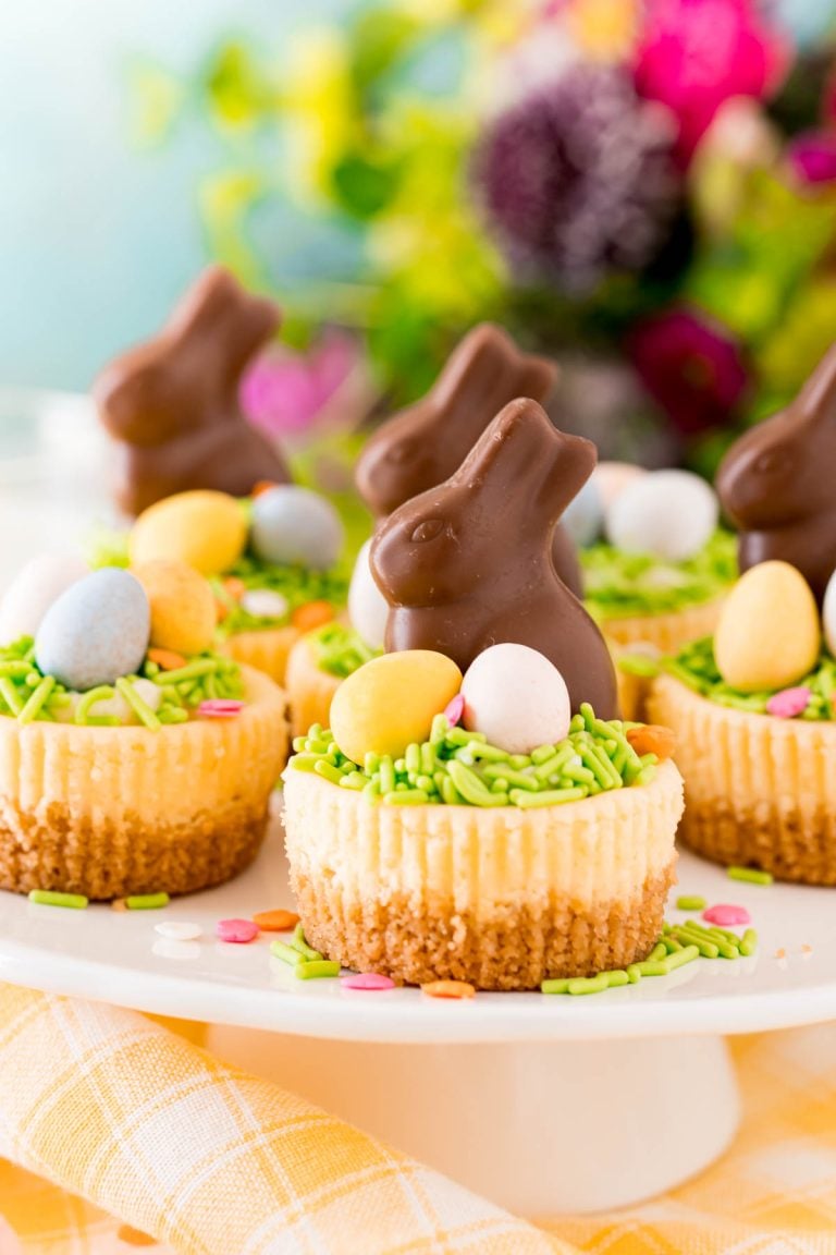 Easter cheesecakes topped with cadbury eggs and chocolate bunnies on a white cake stand.