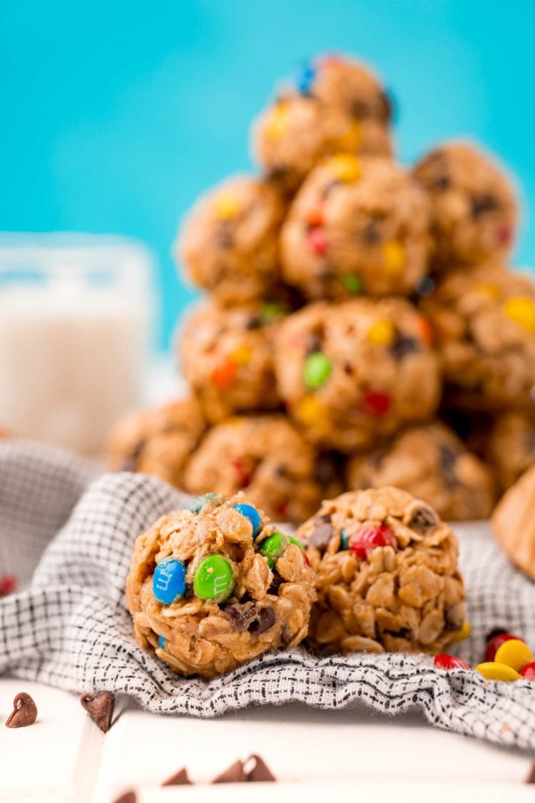 Close up photo of monster cookie energy balls on a table with a plate of them in the background with a glass of milk.