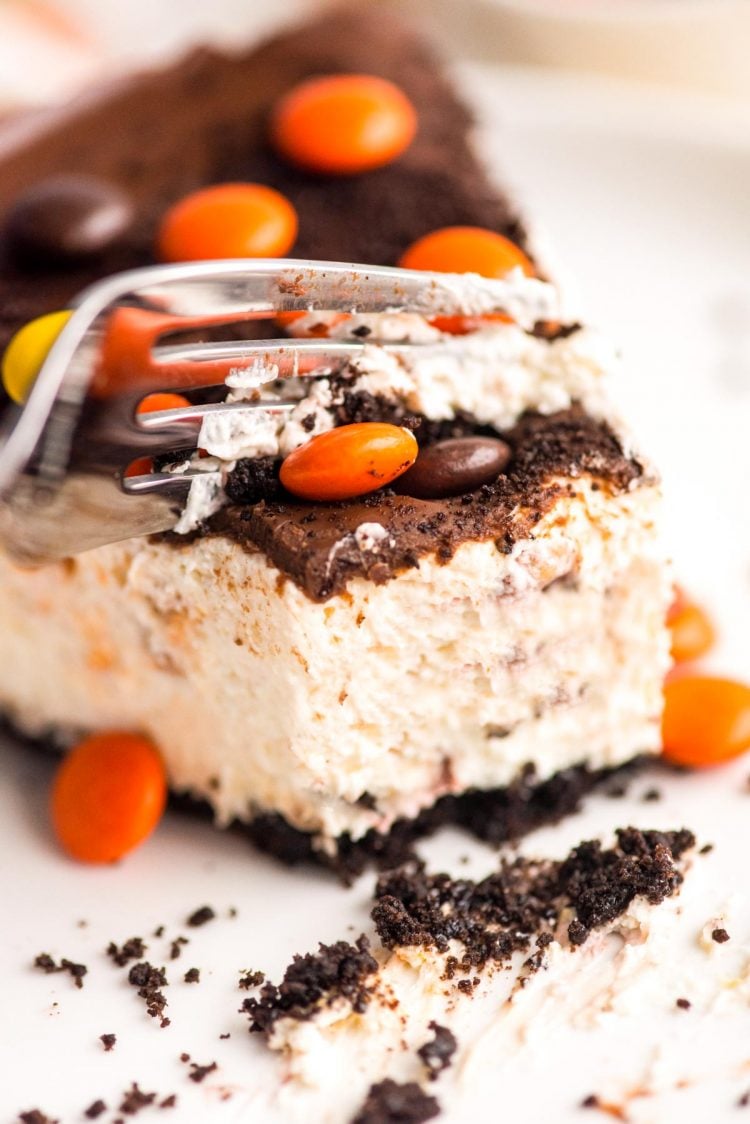 Close up photo of a no bake peanut butter cheesecake on a white plate with a fork cutting a piece off.