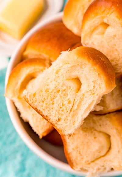 Close up photo of parker house rolls piled in a white bowl on a teal napkin.