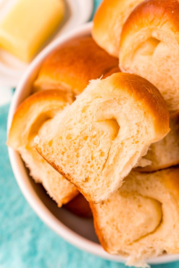 Close up photo of parker house rolls piled in a white bowl on a teal napkin.