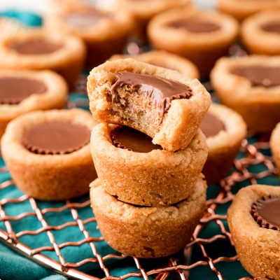 Close up photo of peanut butter cookie cups stacked on a wire rack and the top one is missing a bite.