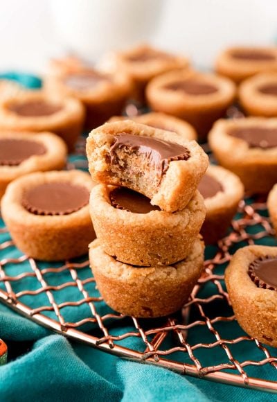 Close up photo of peanut butter cookie cups stacked on a wire rack and the top one is missing a bite.