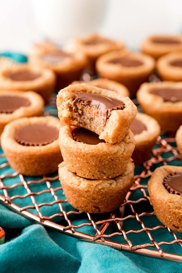 Close up photo of a stack of three peanut butter cookie bites on a copper wire rack with more in the background. The top cookie is missing a bite.