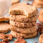 Close up photo of pecan sandies stacked on top of each other with a bite taken out of the top one.