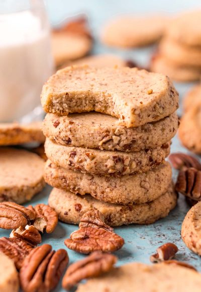 Close up photo of pecan sandies stacked on top of each other with a bite taken out of the top one.