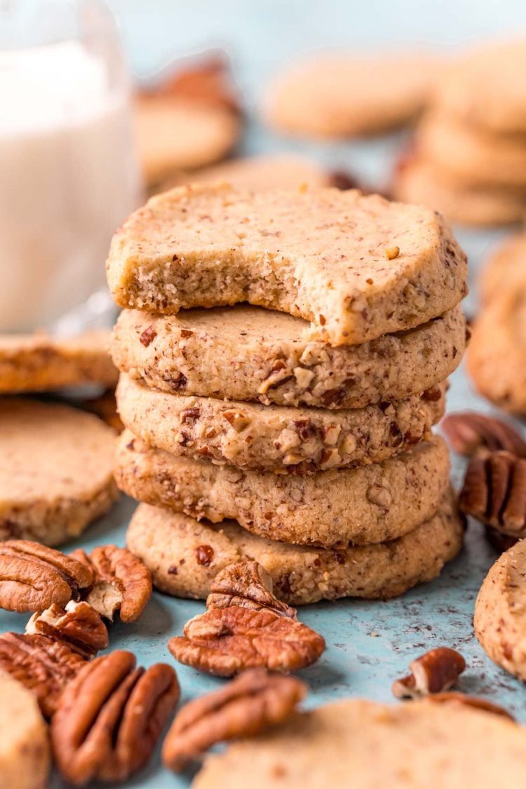 Close up photo of pecan sandies stacked on top of each other with a bite taken out of the top one.