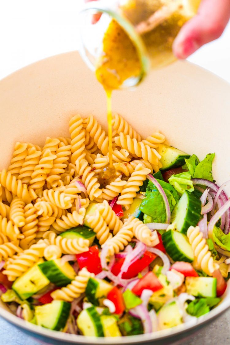 A woman's hand pour dressing into a bowl with ingredients for pasta salad.