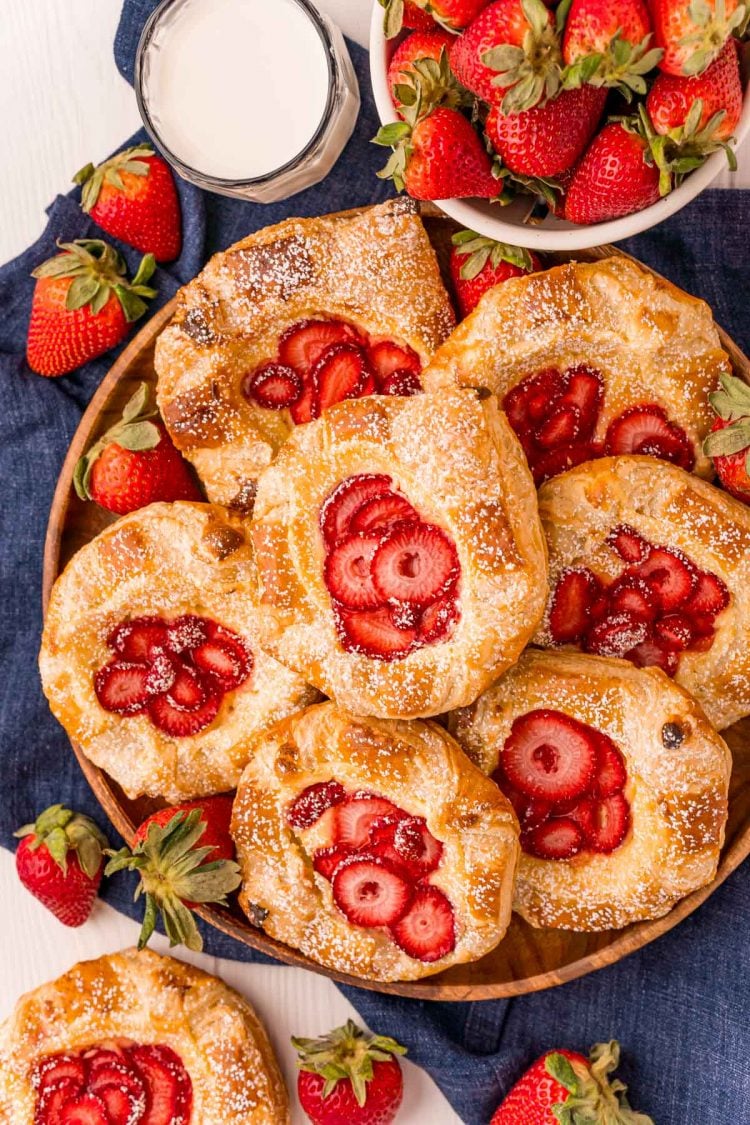 Overhead photo of strawberry cheese danishes on a wooden plate on a blue napkin.