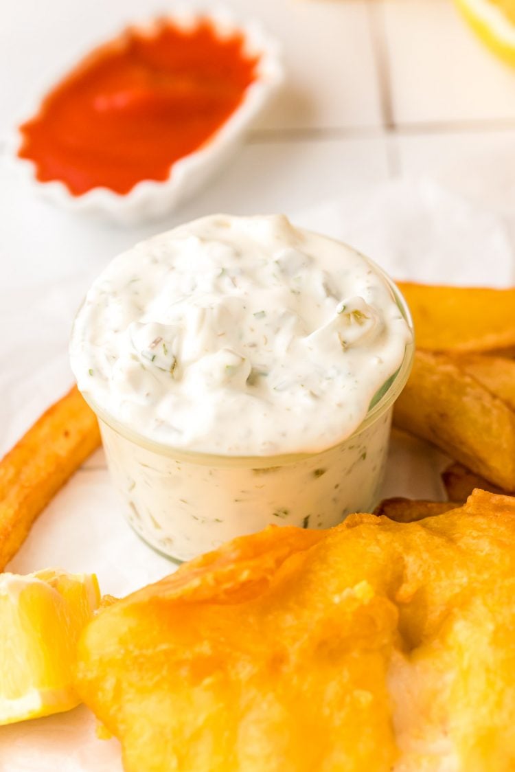 Tartar Sauce in a jar next to fried fish and chips.