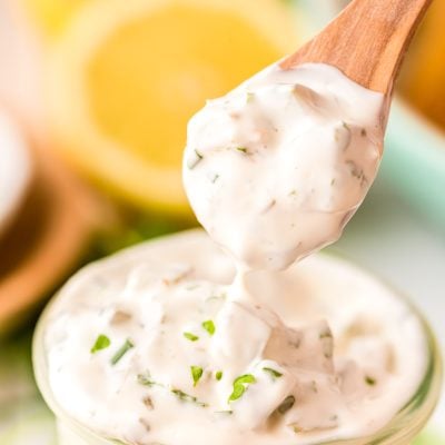 A spoon scooping tartar sauce out of a jar.