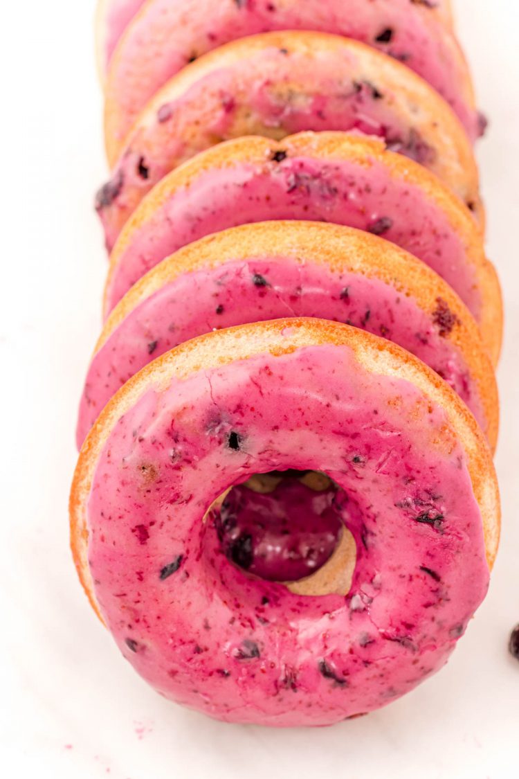 Close up photo of blueberry donuts in a row on a white counter top.