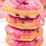 Close up photo of a stack of four blueberry donuts on a marble plate.