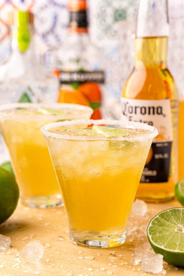 Close up photo of Beergaritas on a wooden cutting board with limes and bottles in the background. 