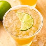 Close up photo og a glass with a beer margarita in it rimmed with sugar and garnished with lime wedges.