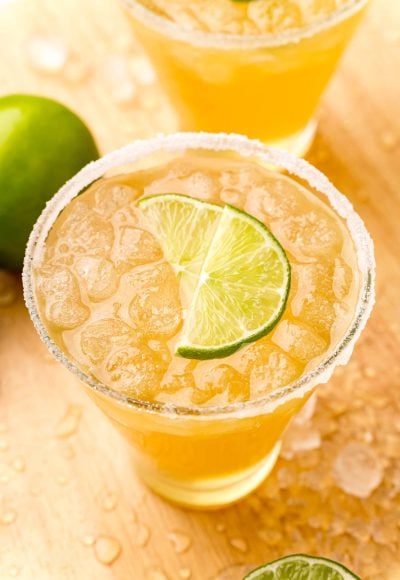 Close up photo og a glass with a beer margarita in it rimmed with sugar and garnished with lime wedges.