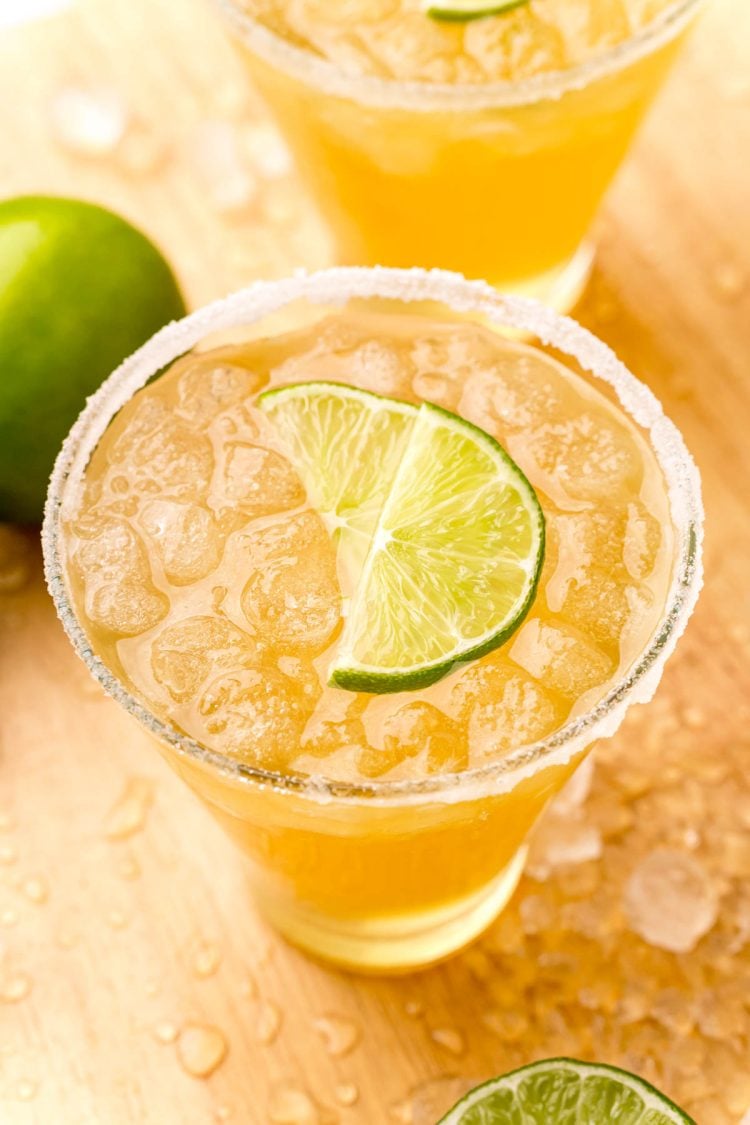 Close up photo og a glass with a beer margarita in it rimmed with sugar and garnished with lime wedges.