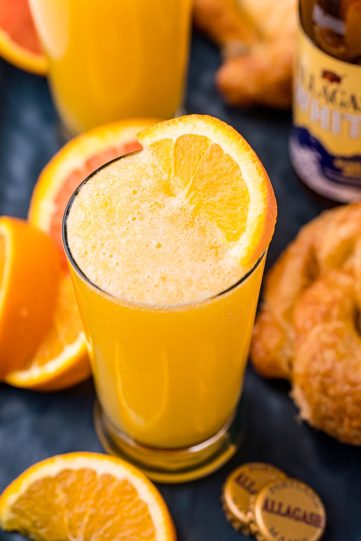 Close up photo of a beermosa surrounded by orange slices and croissants.