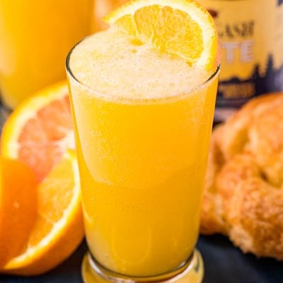 Close up photo of a beermosa on a blue serving platter with croissants and oranges.