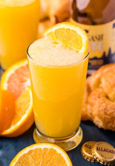 Close up photo of a beermosa on a blue serving platter with croissants and oranges.