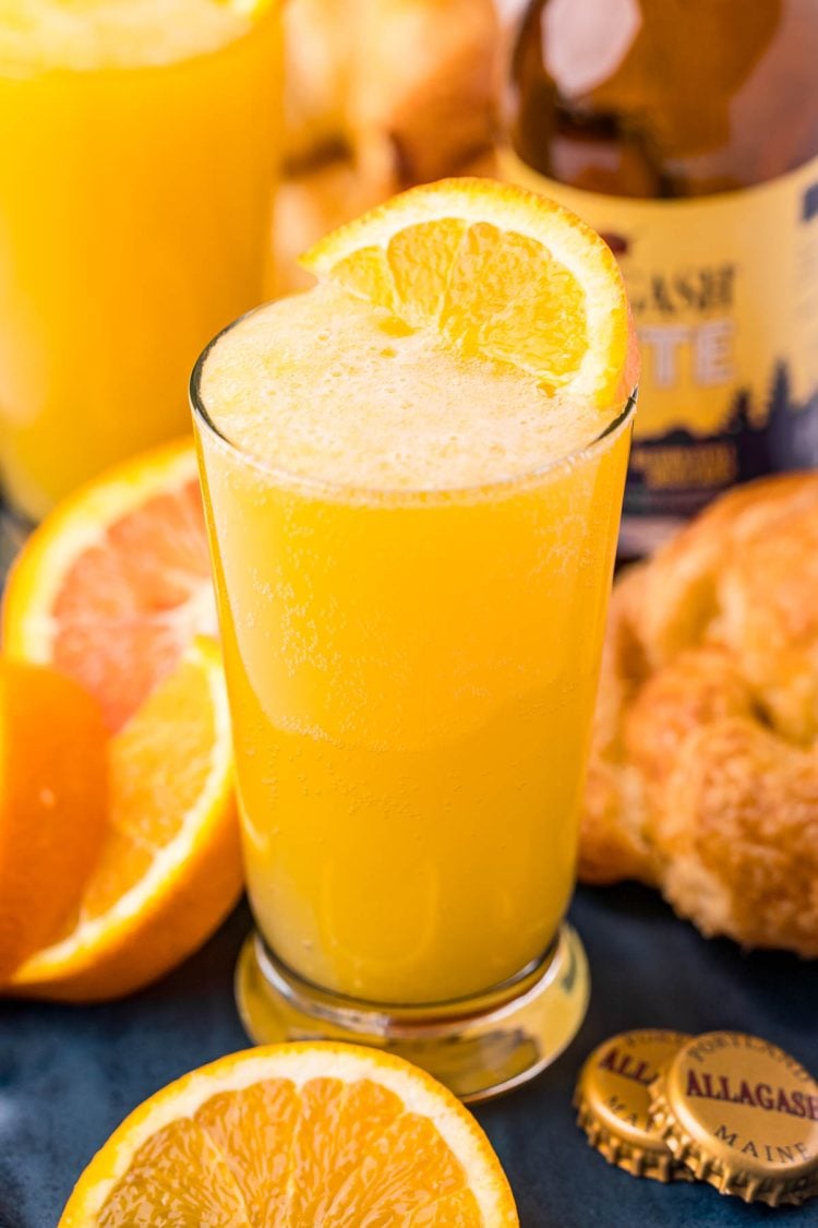 Close up photo of a beermosa on a blue serving platter with croissants and oranges.