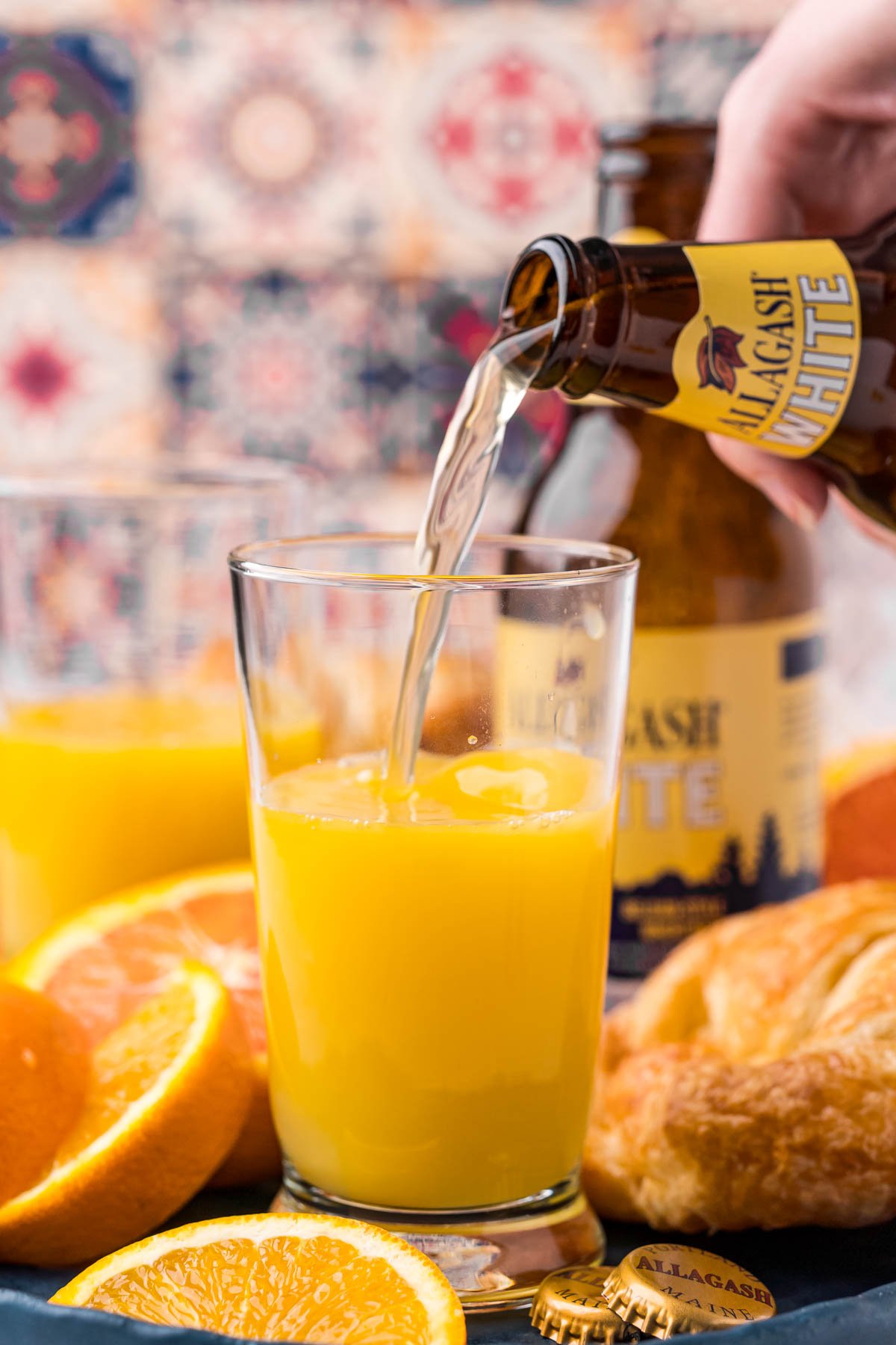 A bottle of beer being poured into a glass with orange juice.