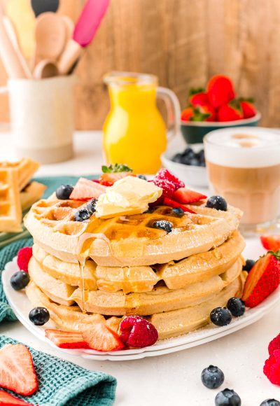 Close up photo of a woman pouring maple syrup over the top of a stack of Belgian waffles.